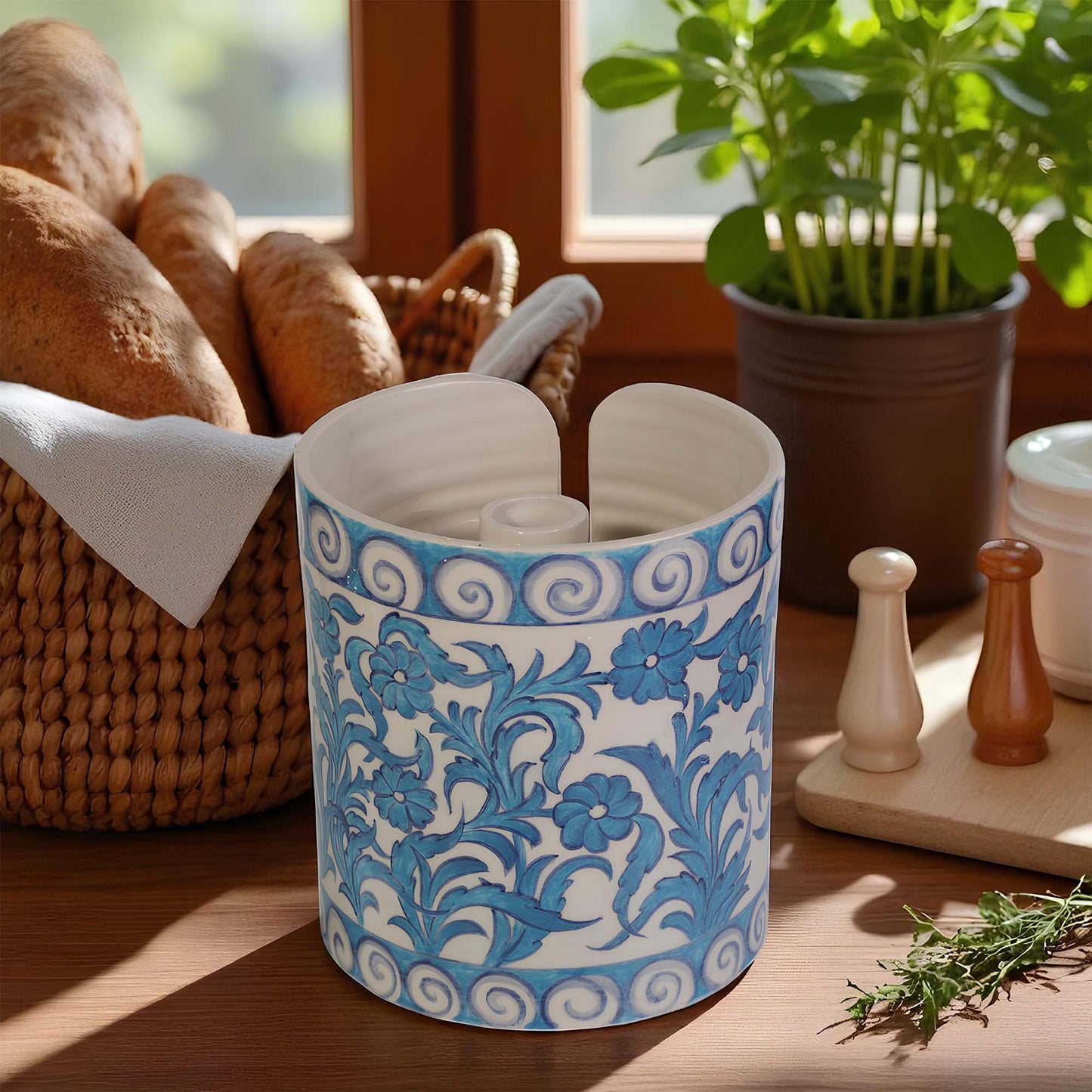 Decorative blue and white ceramic paper towel holder on a wooden surface with plants and bread in the background.