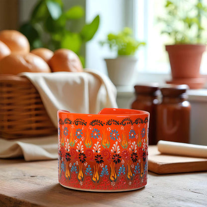 Decorative orange paper towel holder with floral patterns on a wooden surface, with a blurred background of a kitchen setting.