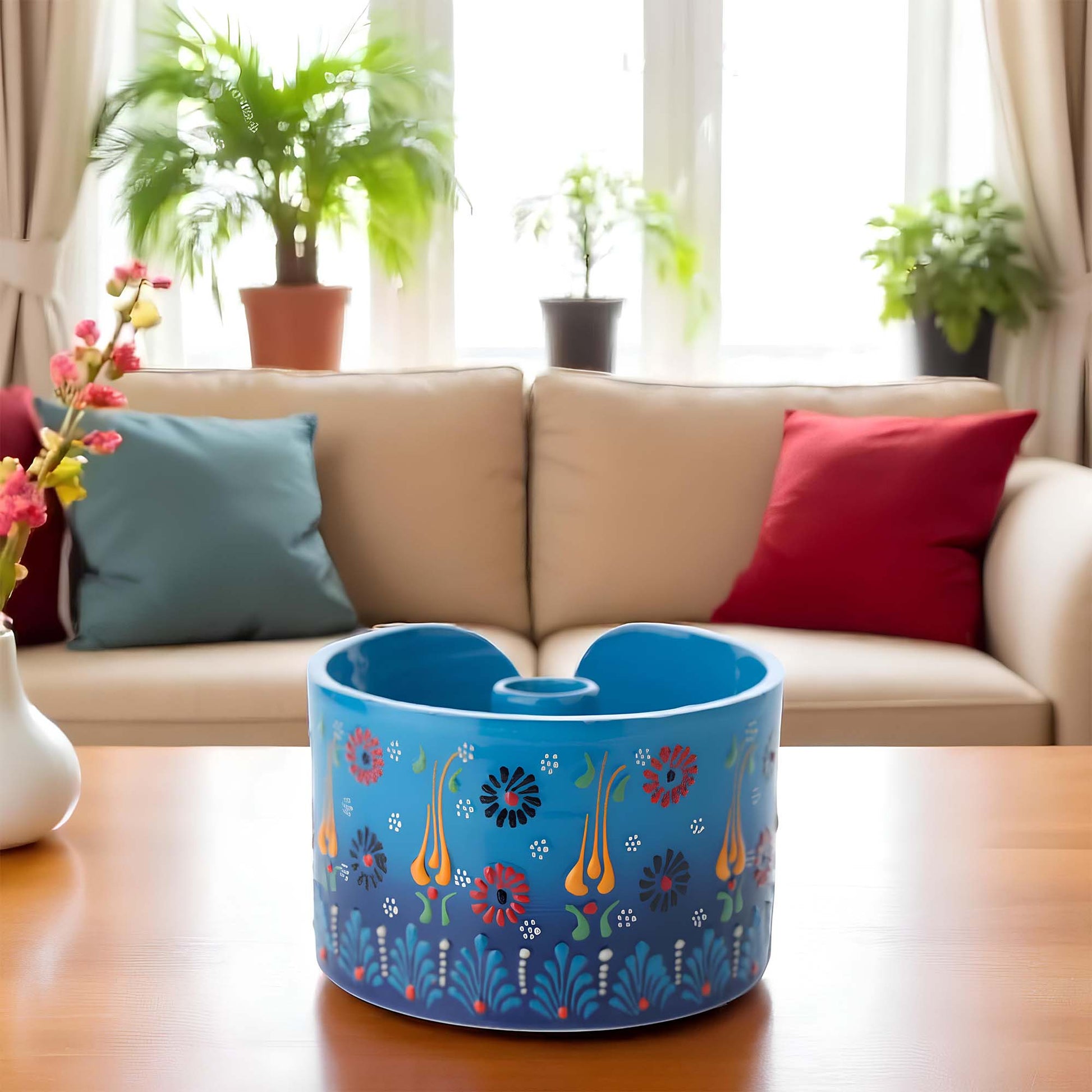 Blue decorative paper towel holder with floral patterns on a wooden table in a living room setting.