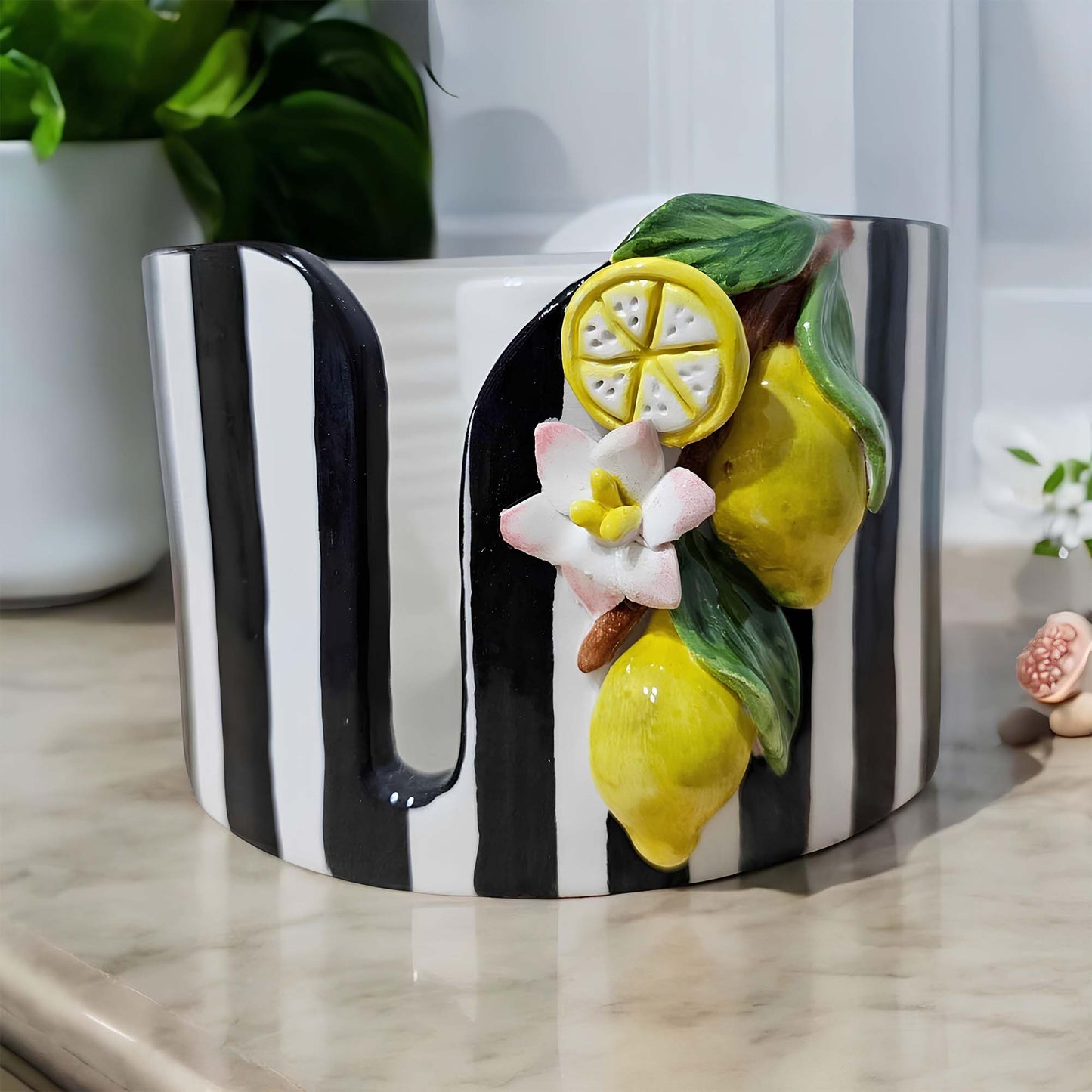 Black and white striped paper towel holder with lemon and flower decorations on a light surface.