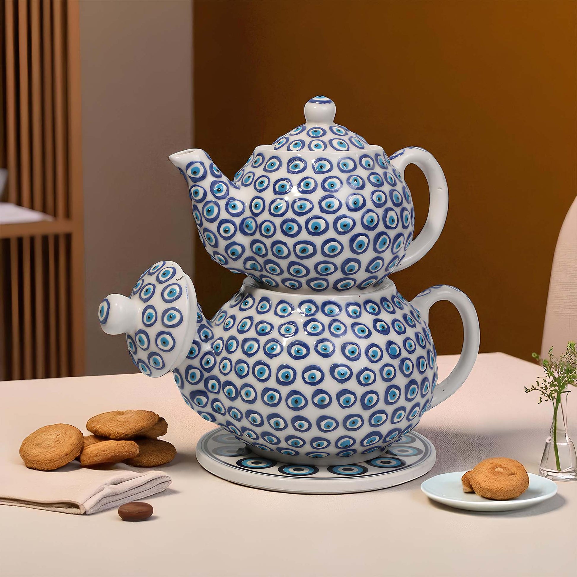 White ceramic teapot with blue circular patterns on a table with cookies and a vase.
