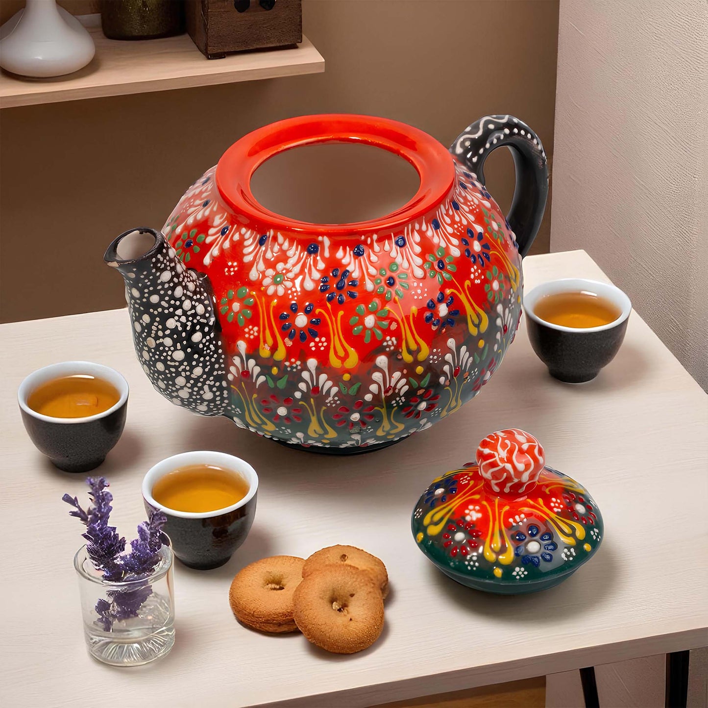 Colorful teapot with floral patterns on a table with tea cups and cookies.