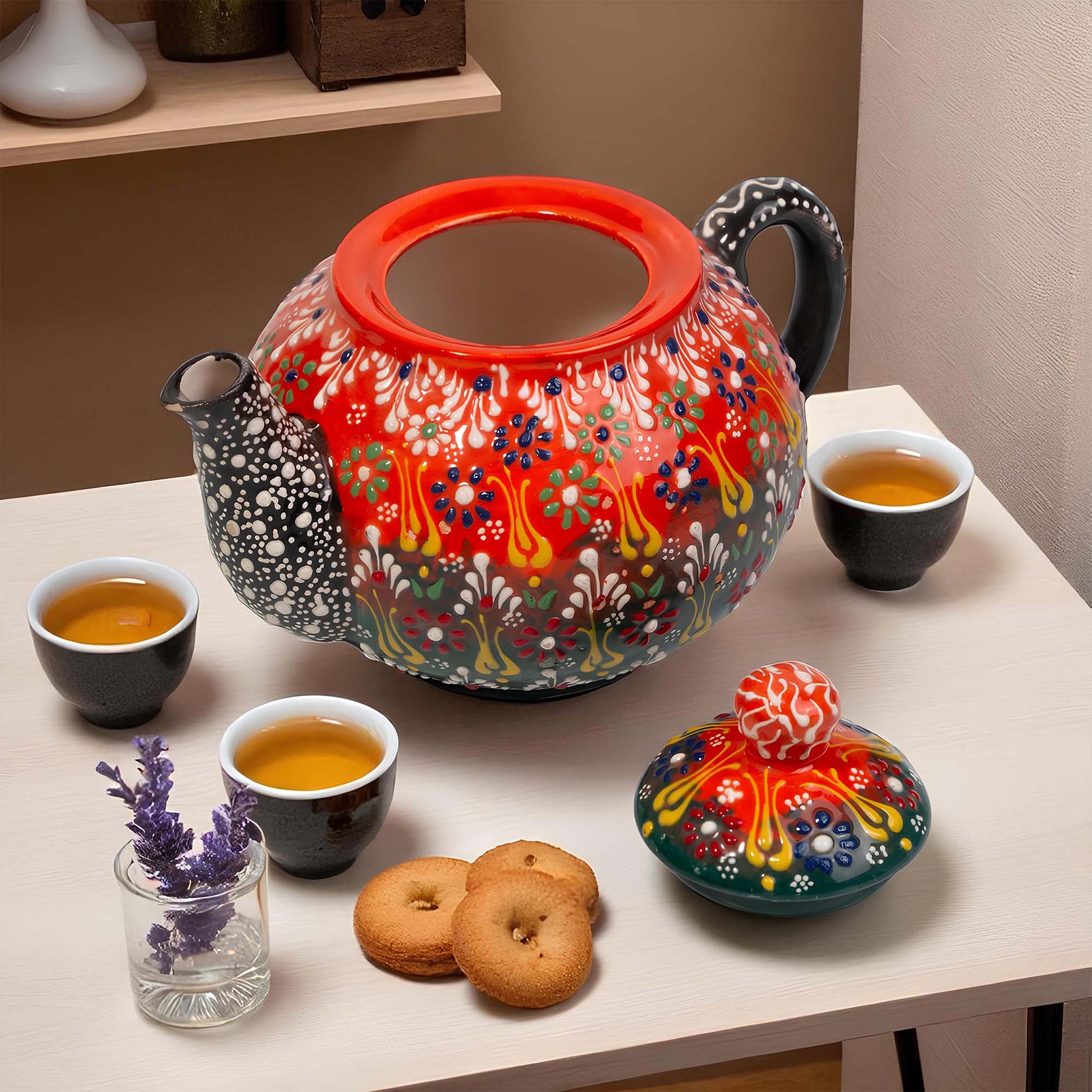 Colorful teapot with floral patterns on a table with tea cups and cookies.