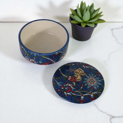 Decorative ceramic sugar bowl with matching lid on a white surface, accompanied by a small potted plant.