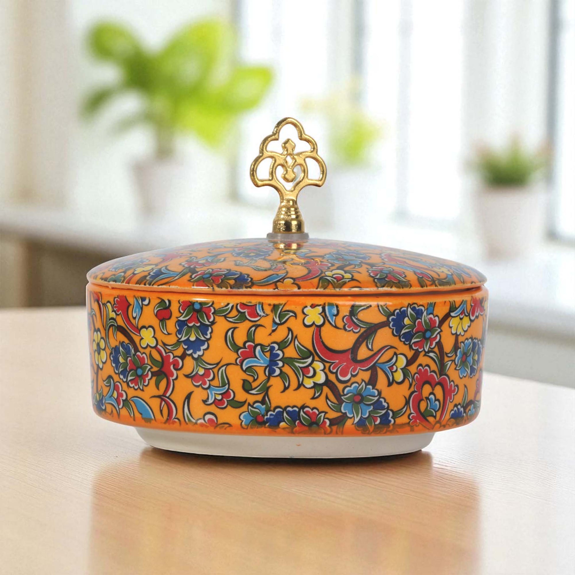 Decorative ceramic sugar bowl with floral patterns and a gold lid on a wooden surface.