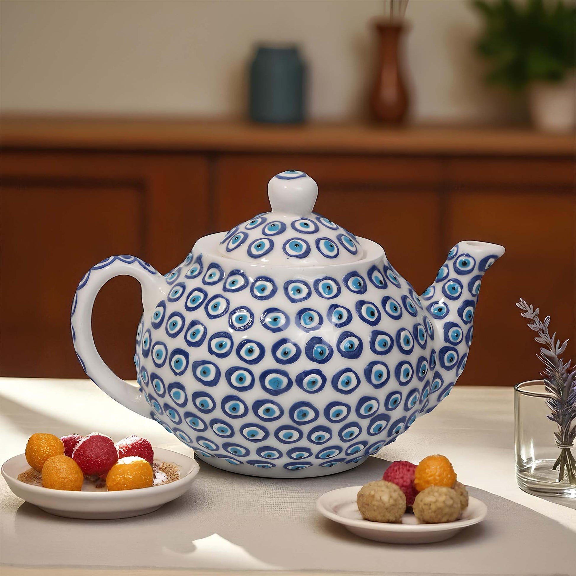 Blue and white patterned teapot on a table with plates of food and a glass.