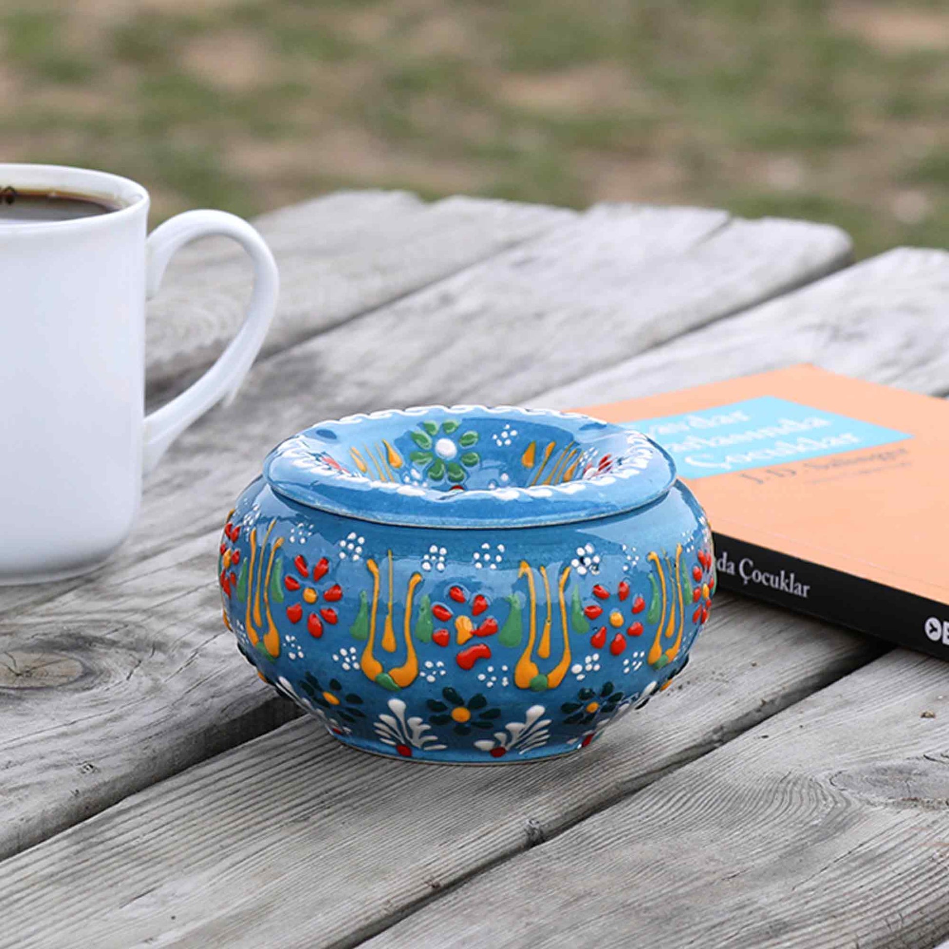 Decorative blue ceramic ashtray with colorful patterns on a wooden surface next to a white mug.
