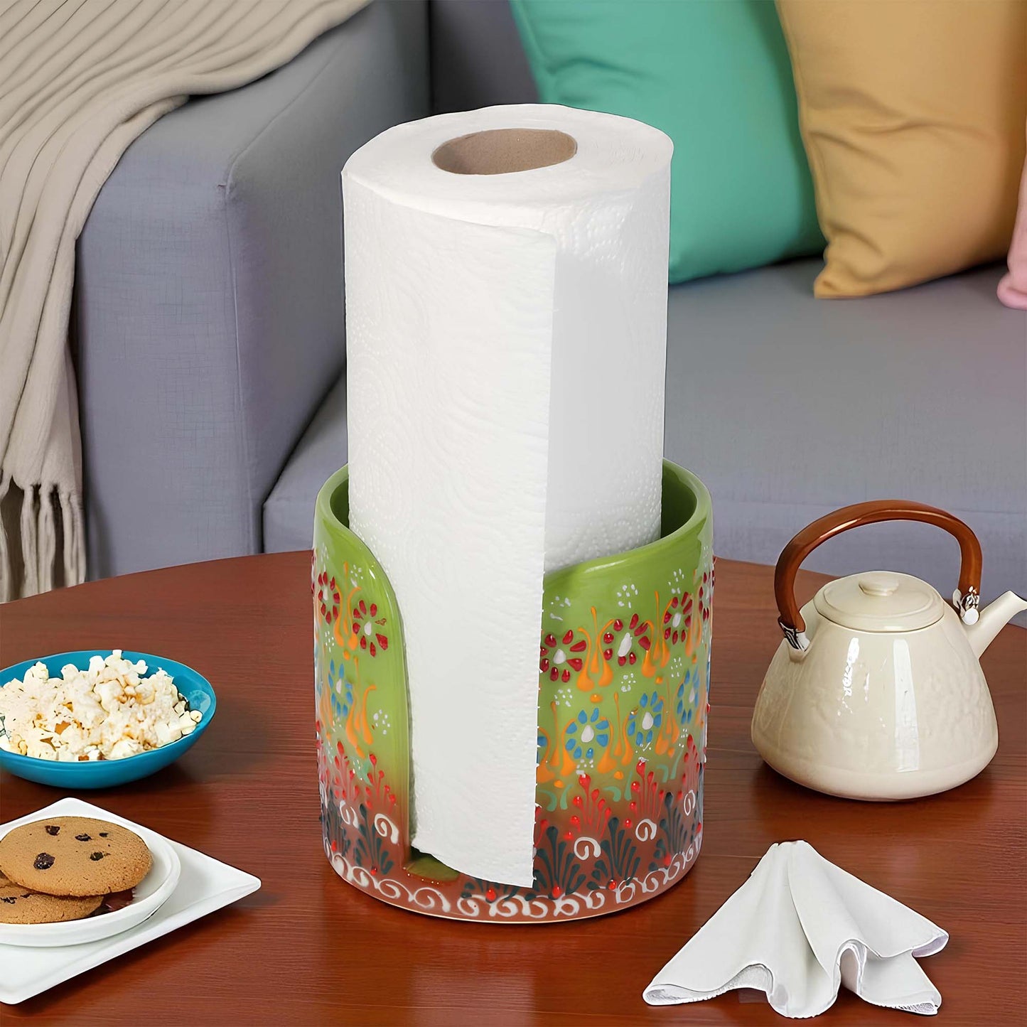 Decorative paper towel holder with a roll of paper towels on a table with snacks and a teapot.