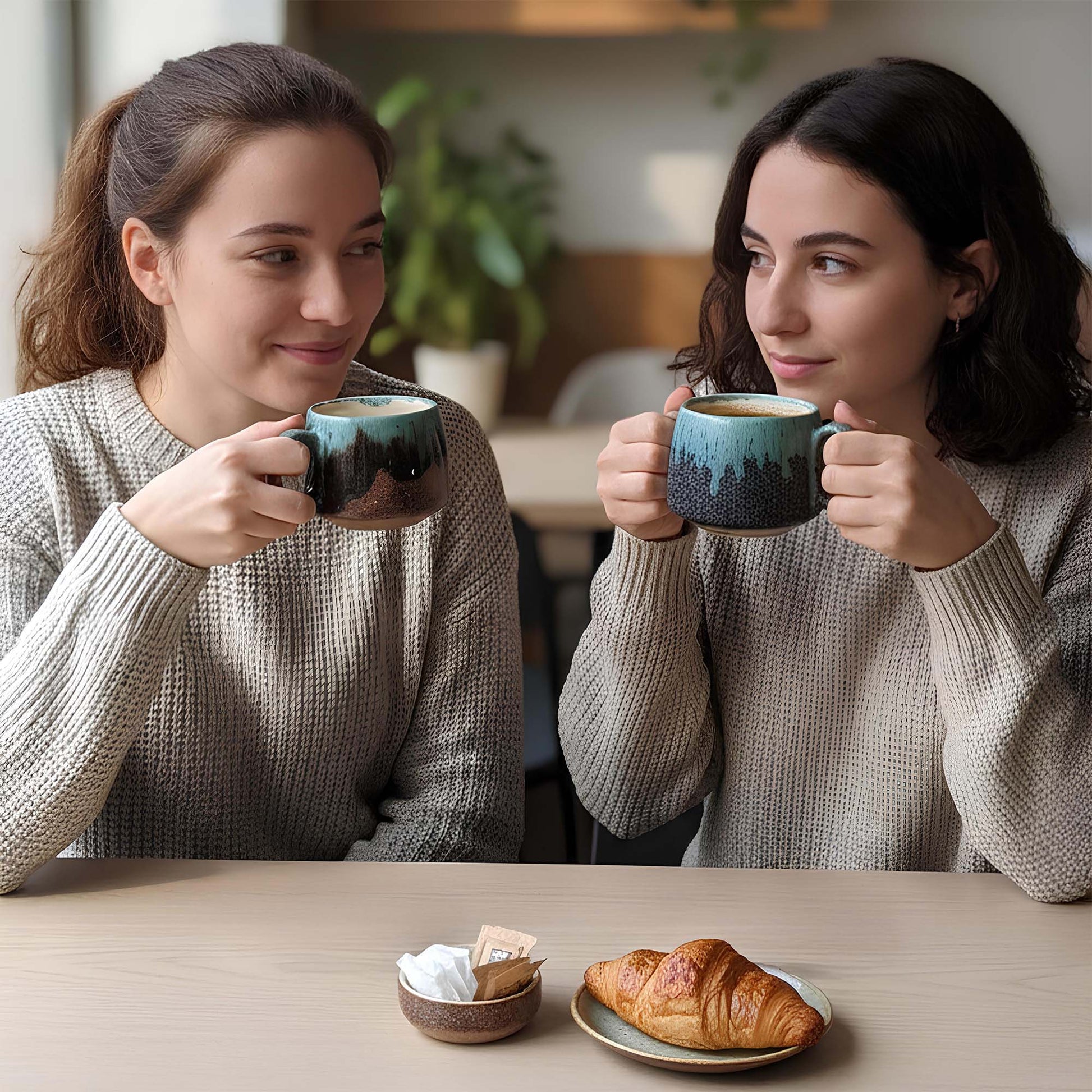 Two women sitting at a table with coffee mugs and pastries.