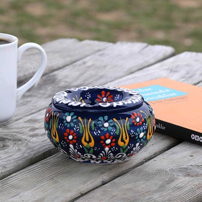 Decorative ceramic ashtray with floral patterns on a wooden surface next to a white mug.