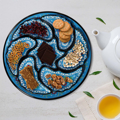 Decorative snack serving tray set with various snacks on a white surface with a teapot and cup of tea.