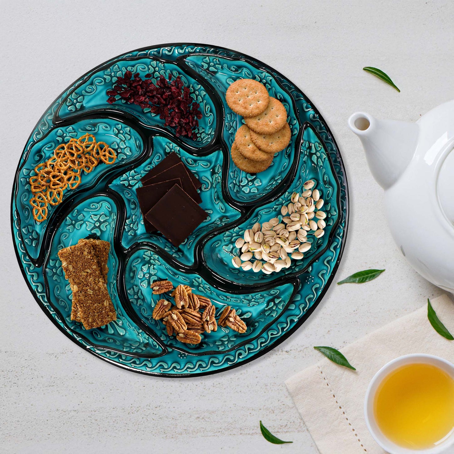Decorative snack serving tray setwith assorted snacks on a white surface with a teapot and cup of tea.