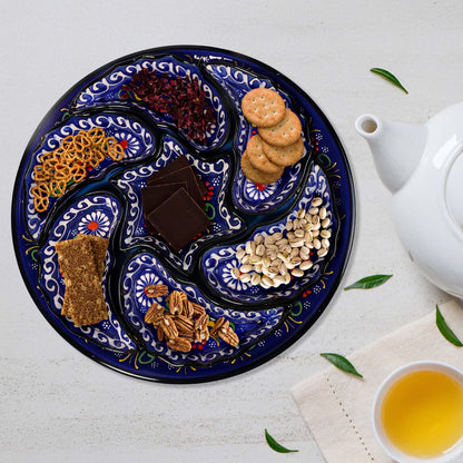 Decorative snack serving tray set with assorted snacks on a white surface with a teapot and cup of tea.