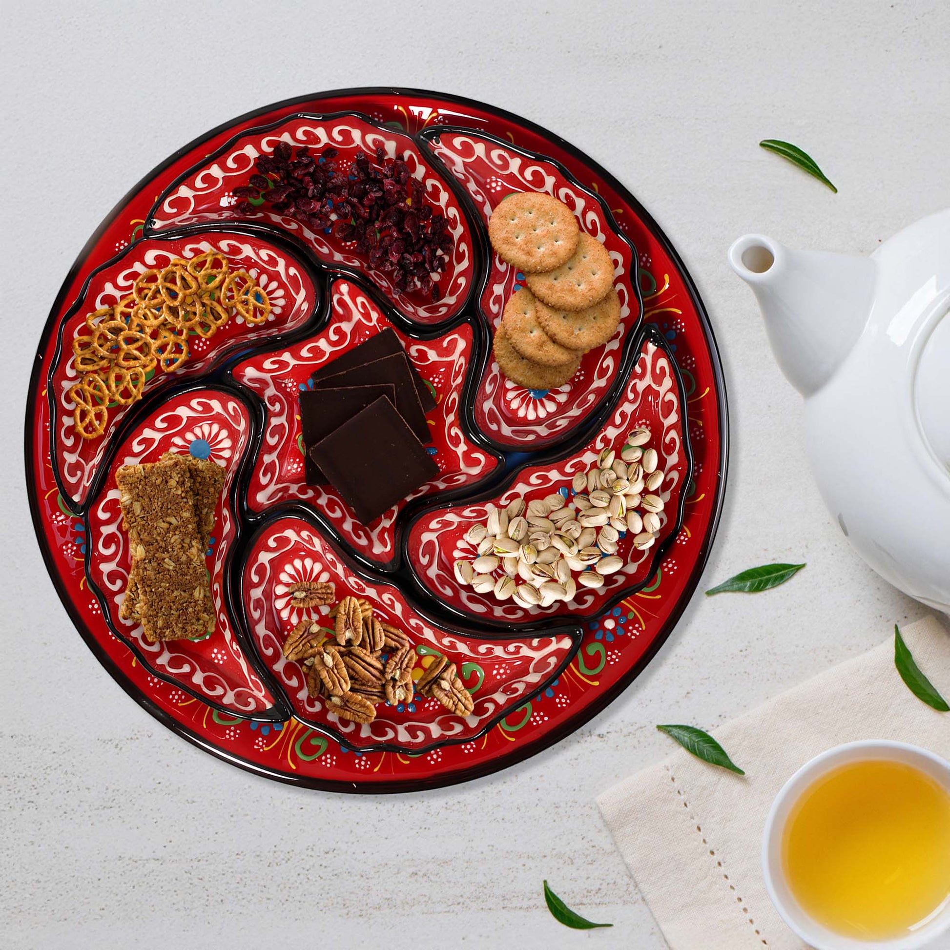 Decorative snack serving tray set with assorted snacks on a white surface with a teapot and cup of tea.