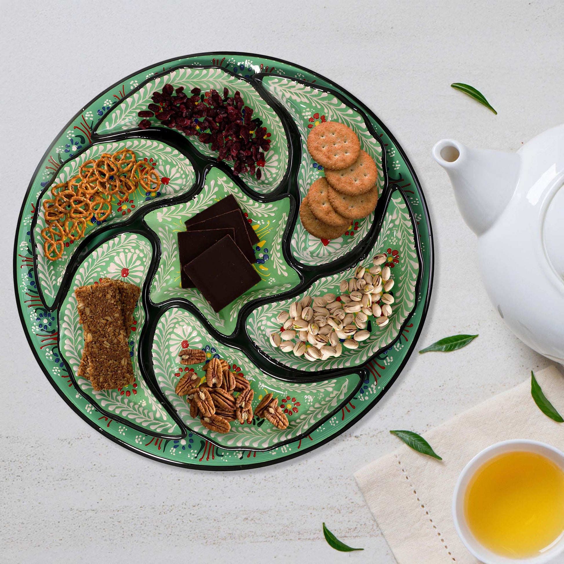 Decorative snack serving tray set with various snacks on a white surface with a teapot and cup of tea.