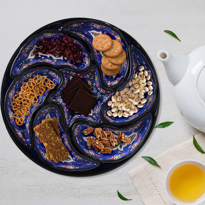 Decorative tray with various snacks on a white surface with a teapot and cup.