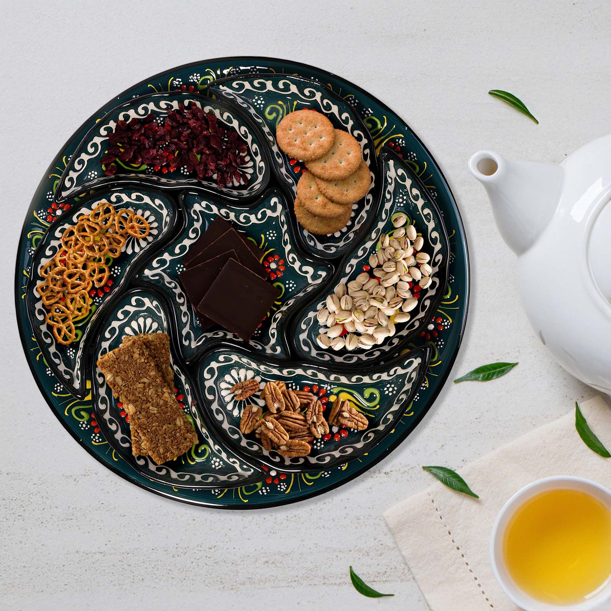 Decorative snack serving tray set with assorted snacks on a white surface with a teapot and cup.