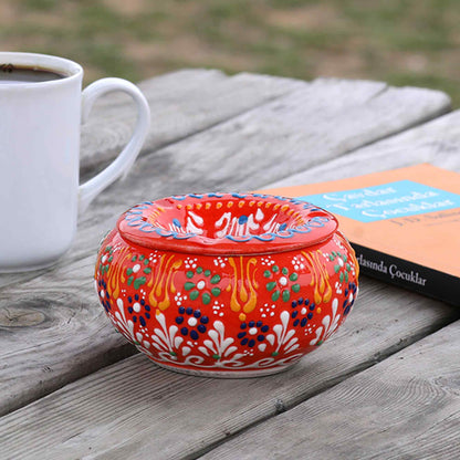 Decorative ceramic ashtray with colorful patterns on a wooden surface next to a white mug and book.