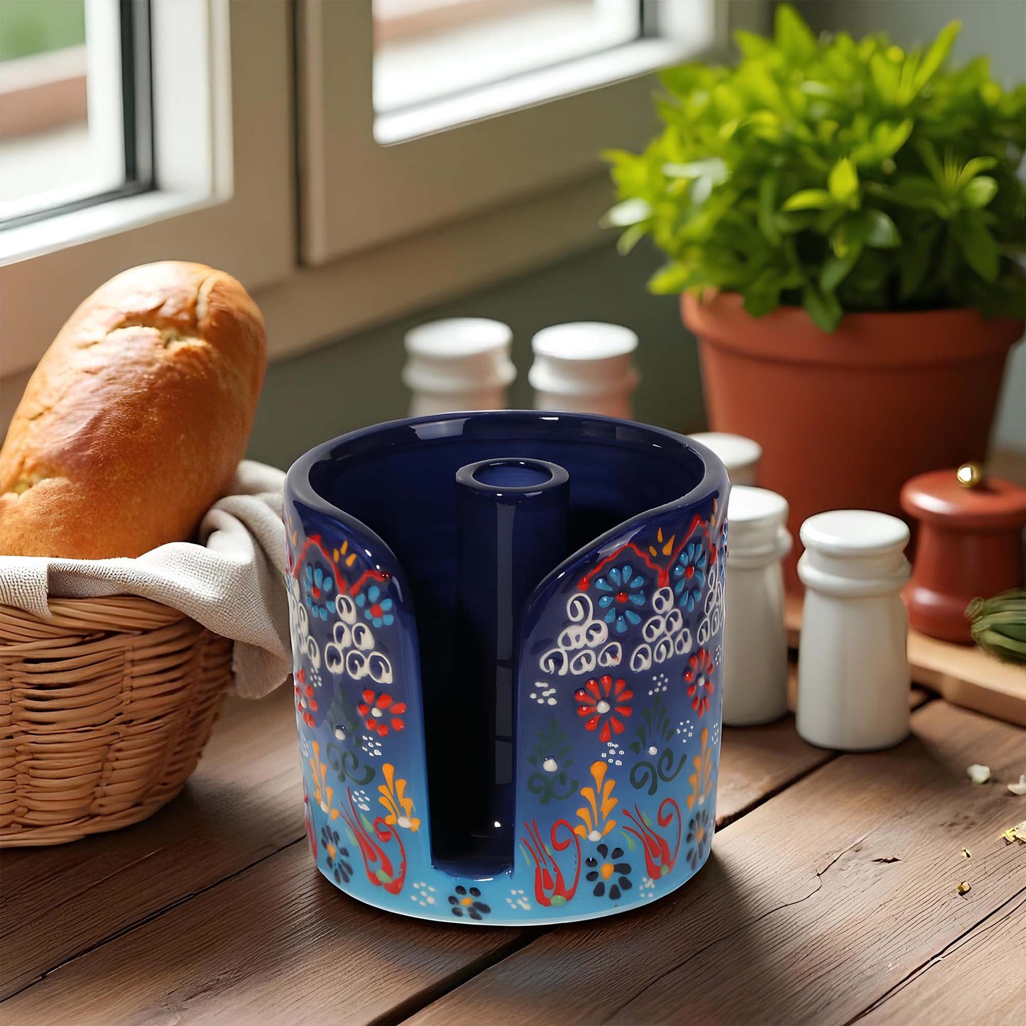 Decorative blue paper towel holder with floral patterns on a wooden surface with bread and plants.
