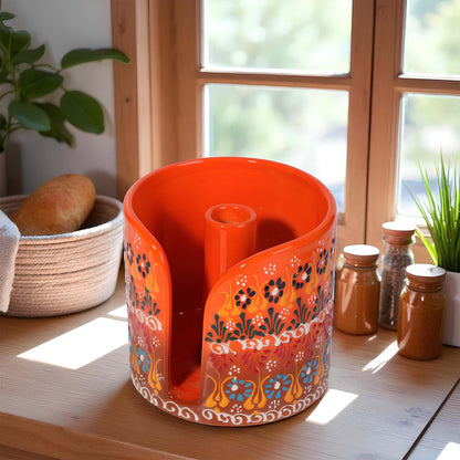 Decorative orange paper towel holder  with floral patterns on a wooden surface near a window.