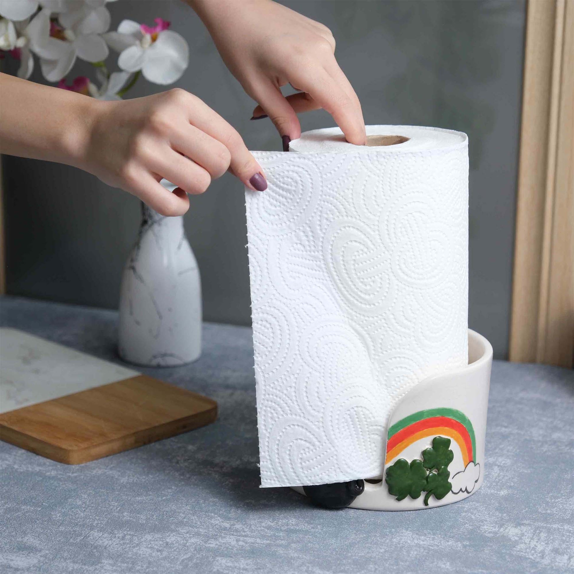 Person pulling a roll of paper towel from a paper towel holder with a rainbow and clover design.