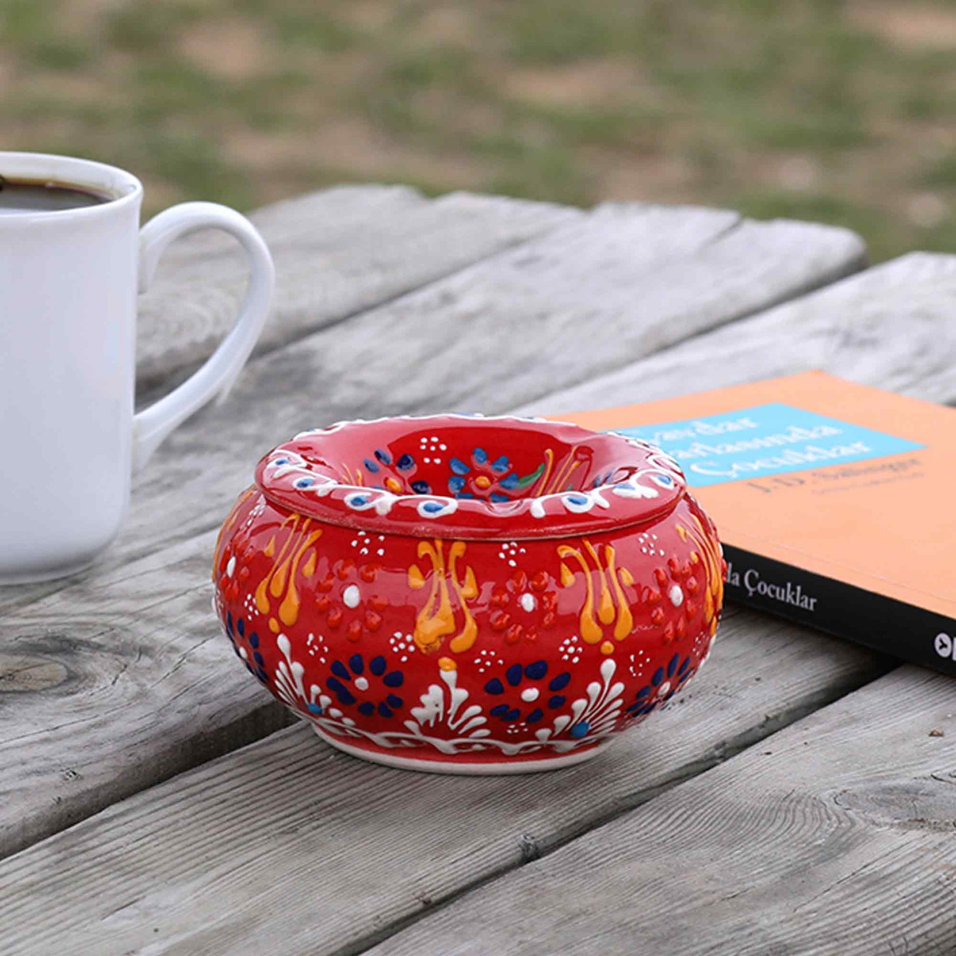 Colorful ceramic ashtray on a wooden surface with a white mug and book in the background.