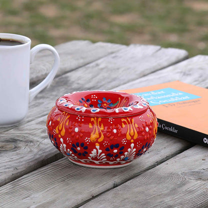 Colorful ceramic ashtray on a wooden surface with a white mug and book in the background.