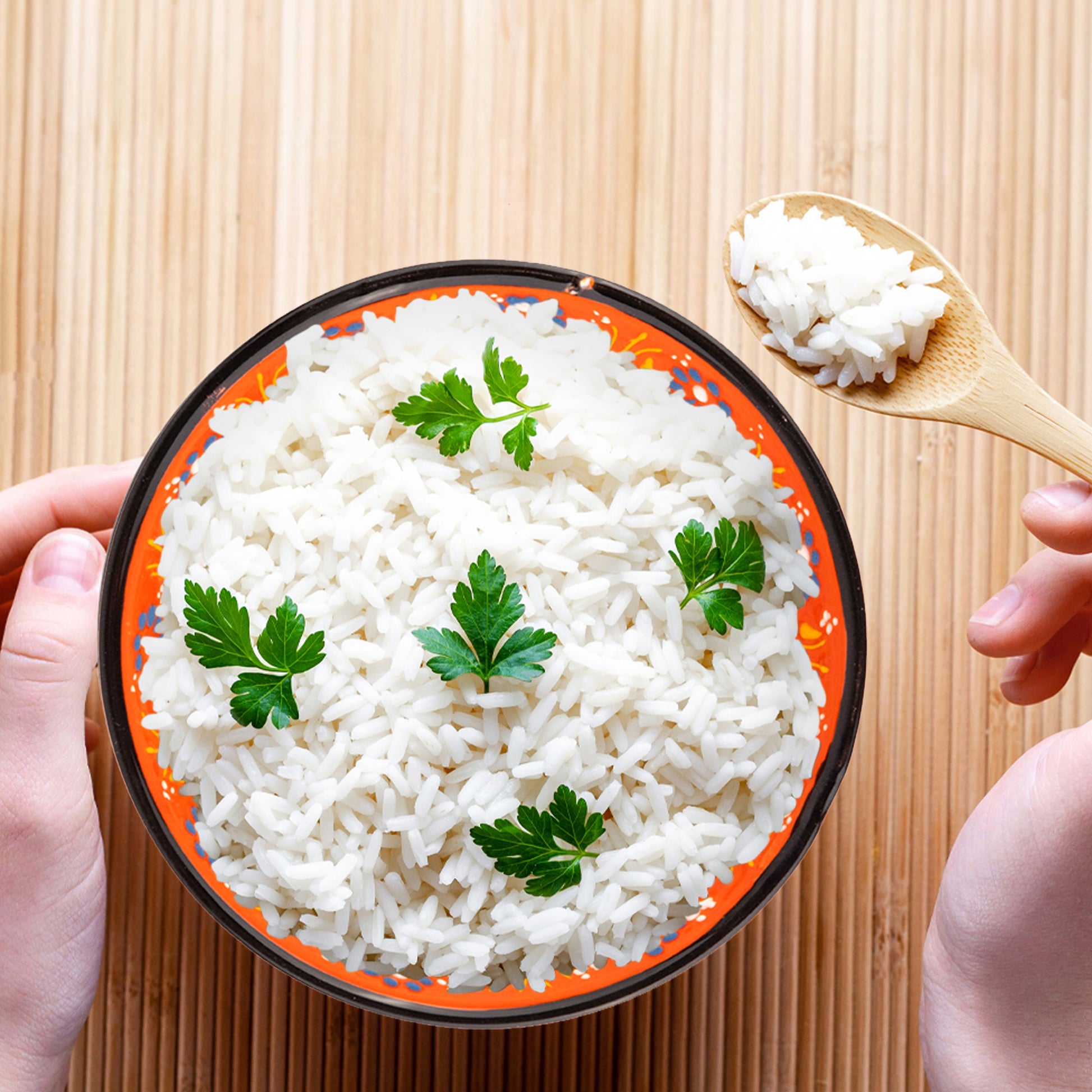 Serving bowl of white rice with green leaves on a wooden surface
