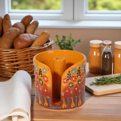 Decorative orange paper towel holder with floral patterns on a kitchen counter with bread and bottles in the background.