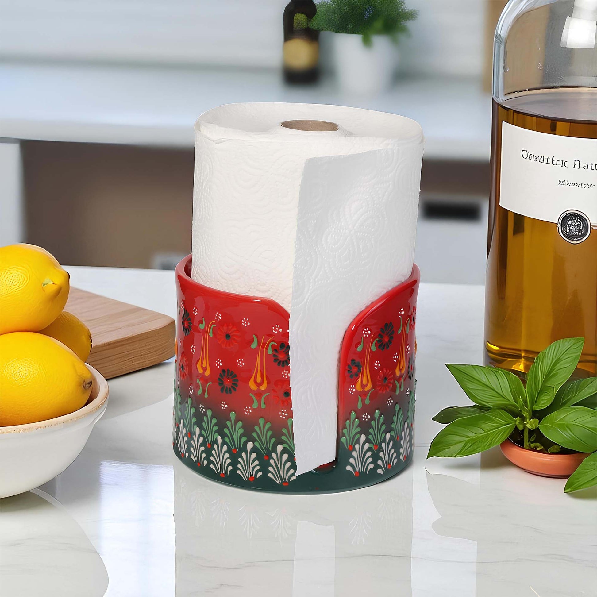 Roll of paper towels in a decorative paper towel holder on a kitchen counter with lemons and a bottle in the background.
