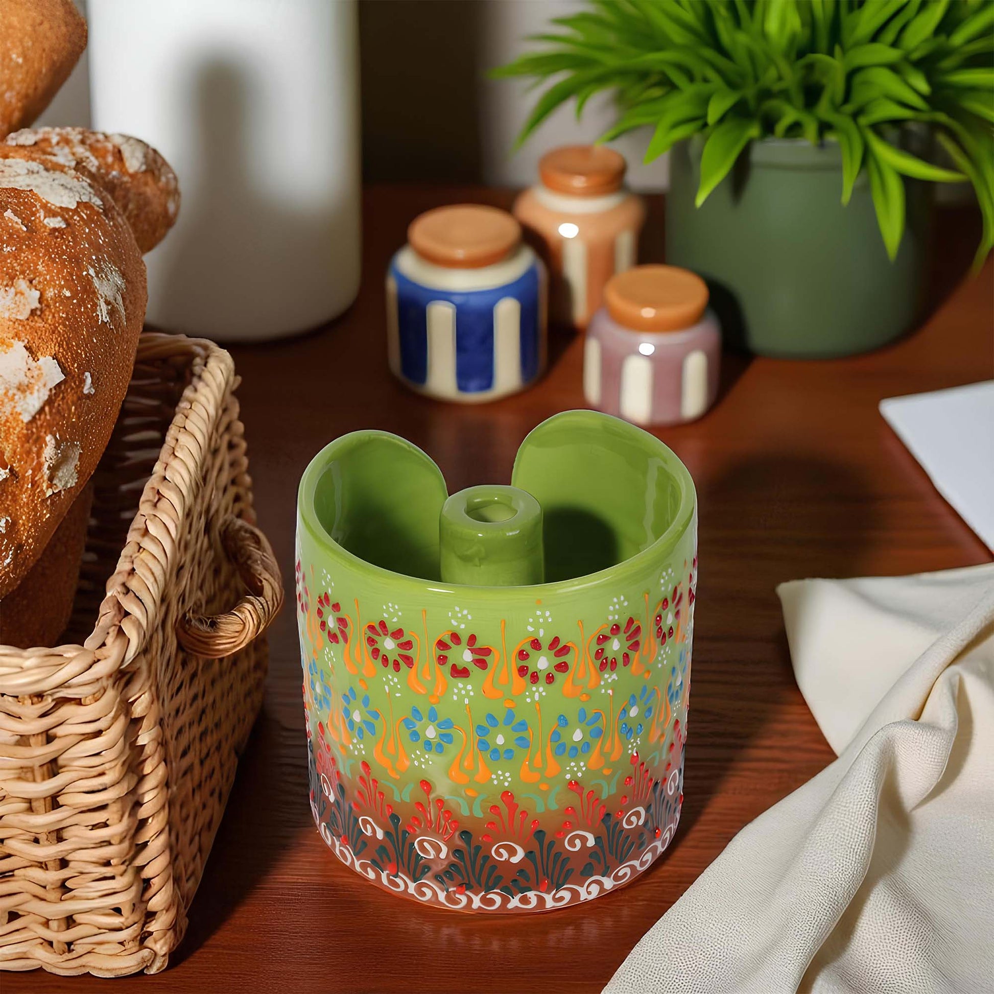 Decorative green paper towel holder with floral pattern on a wooden surface with bread and plants.