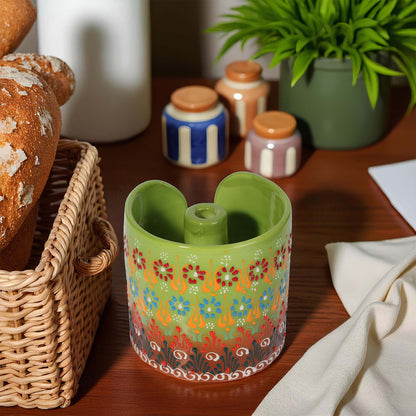 Decorative green paper towel holder with floral pattern on a wooden surface with bread and plants.