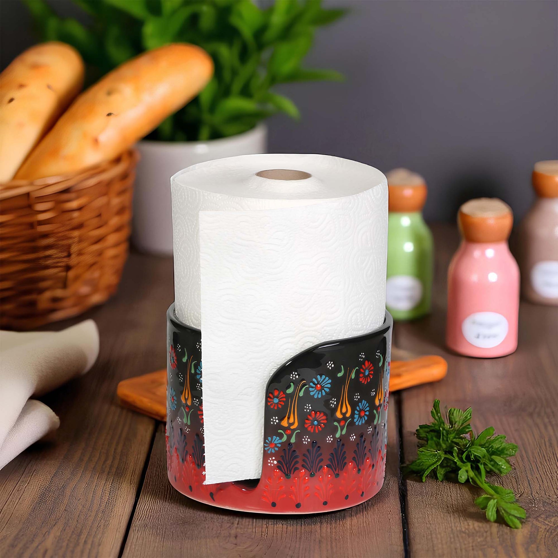 Decorative paper towel holder with a roll of paper towels on a wooden surface with bread and bottles in the background.