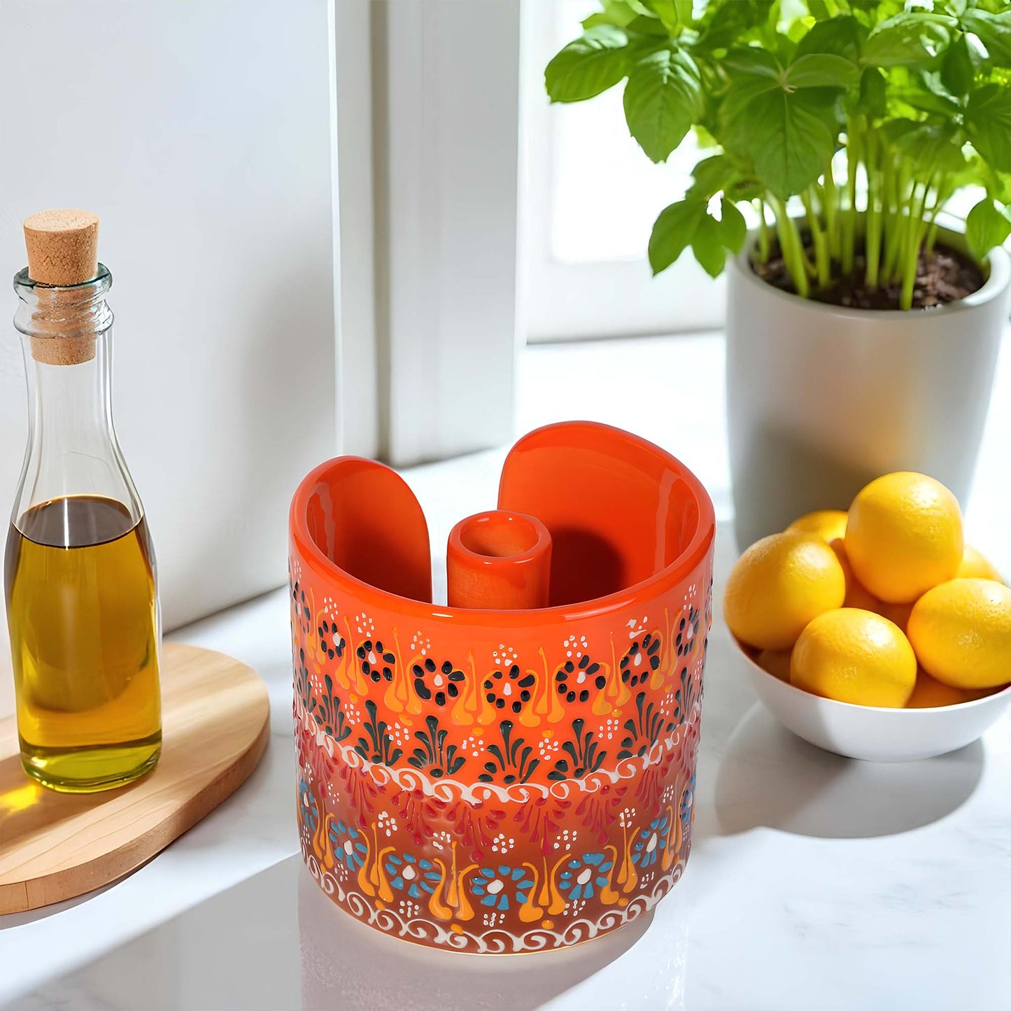Decorative orange paper towel holder with floral patterns on a table with lemons, a bottle, and a plant.