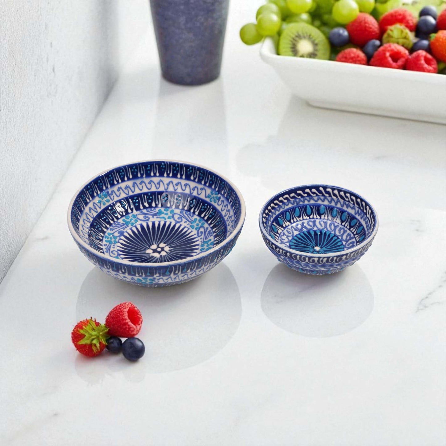 Two blue ceramic bowls with intricate patterns on a white surface with berries and grapes.