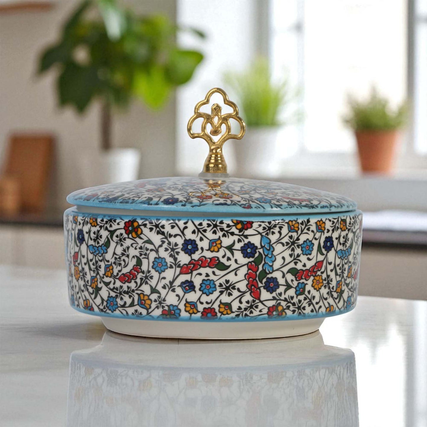 Decorative ceramic sugar bowl with floral patterns and a gold handle on a reflective surface.