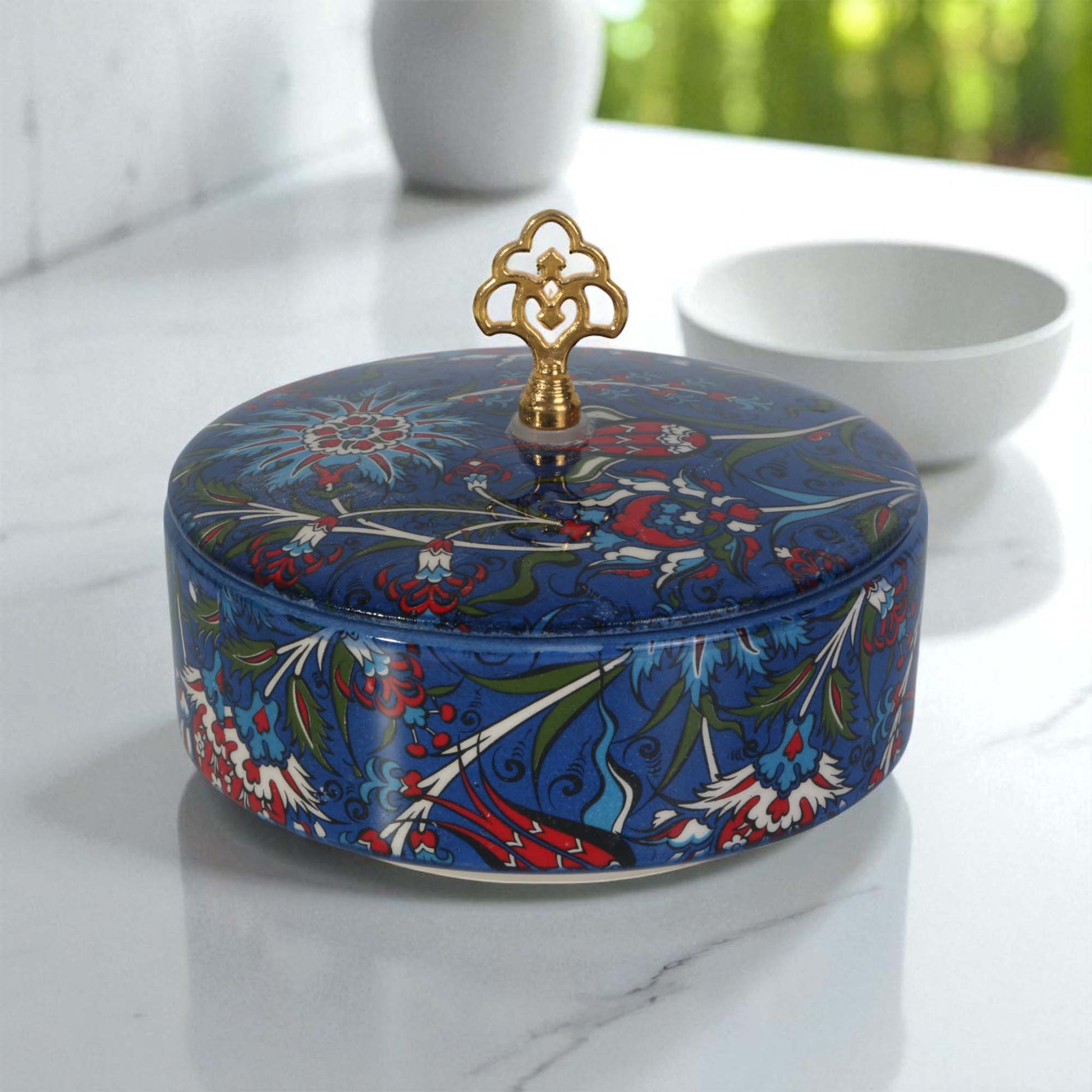 Decorative blue sugar bowl with floral patterns and a gold lid on a marble surface.
