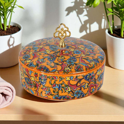Decorative sugar bowl with floral patterns on a wooden surface with plants in the background