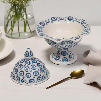 Ceramic sugar bowl with blue and white pattern on a table with a vase and spoon.