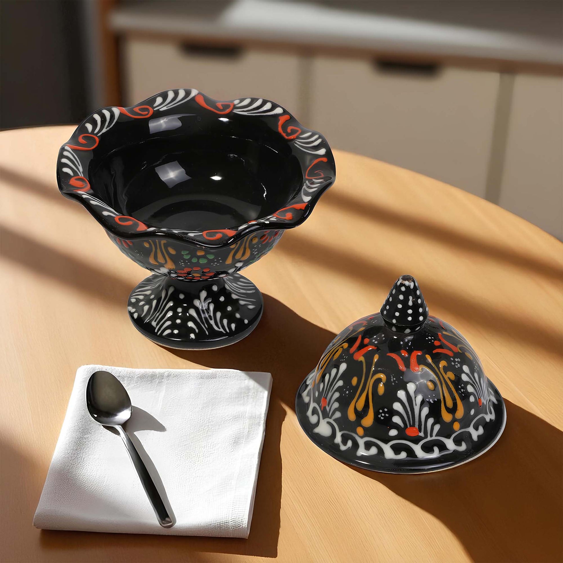 Decorative black sugar bowl with colorful patterns on a wooden table.