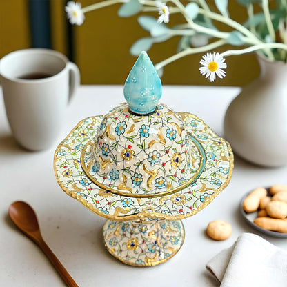 Decorative sugar bowl with floral patterns on a table with a cup, cookies, and flowers.