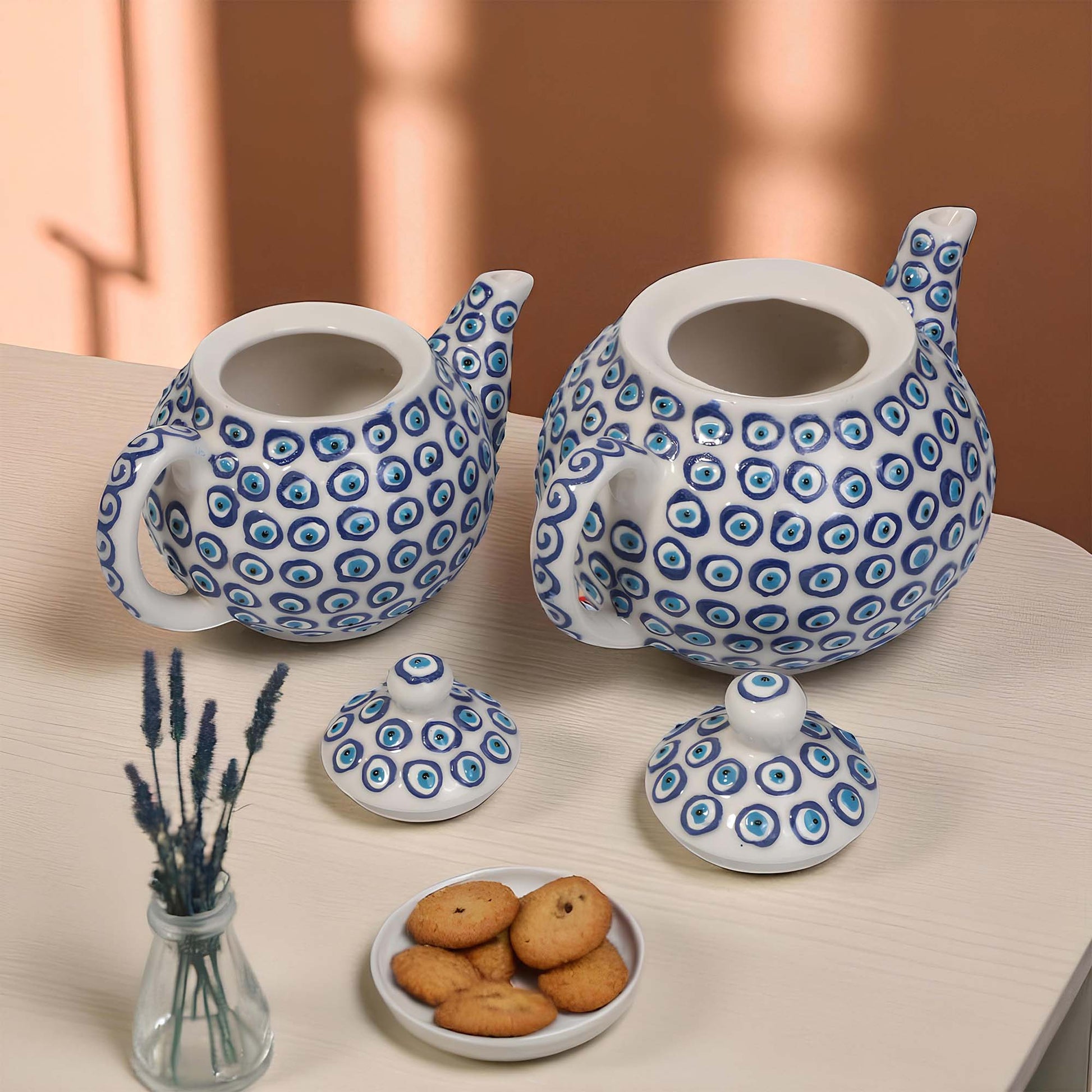 Two ceramic teapots with blue circular patterns on a table with cookies and lavender.
