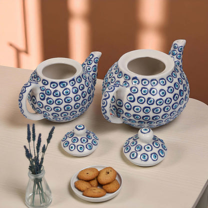 Two ceramic teapots with blue circular patterns on a table with cookies and lavender.