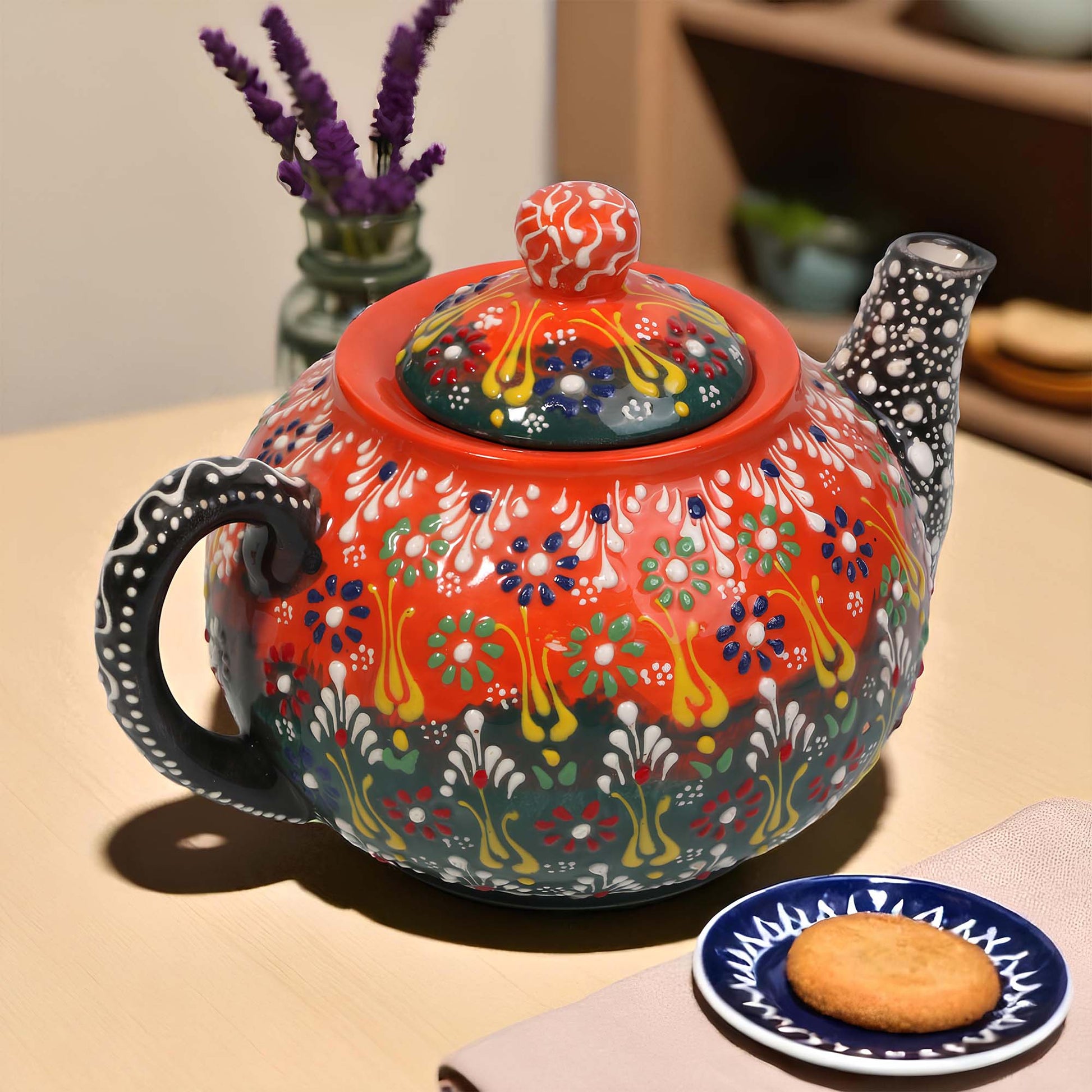 Colorful ceramic teapot with intricate designs on a table with a small plate and cookie.