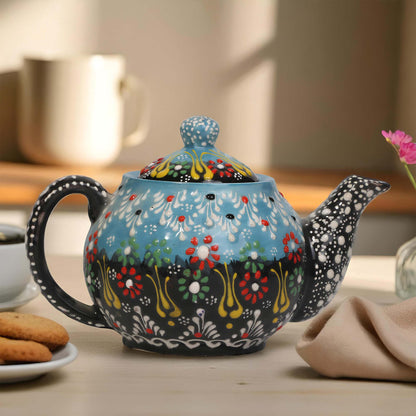 Decorative teapot with floral patterns on a table with cookies and a cup.