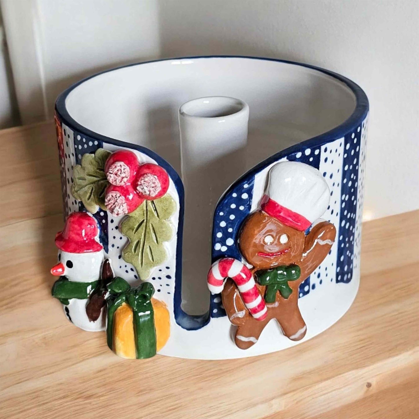 Decorative paper towel holder with gingerbread man and snowman designs on a wooden surface.