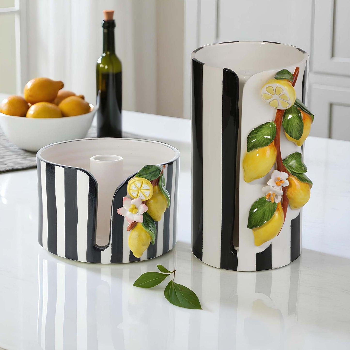Two ceramic paper towel holders with black and white stripes and lemon designs on a kitchen counter.