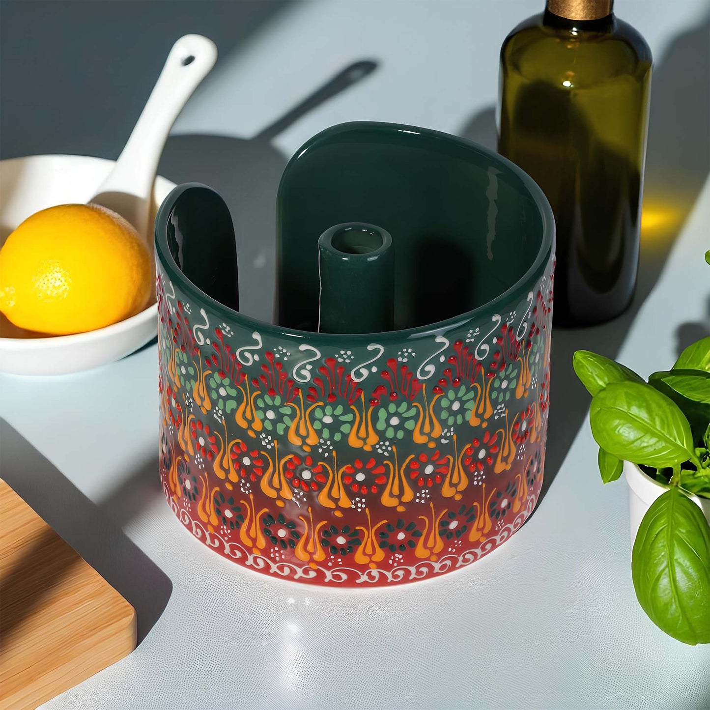 Decorative ceramic paper towel holder with colorful patterns on a kitchen counter with lemon, bottle, and cutting board.