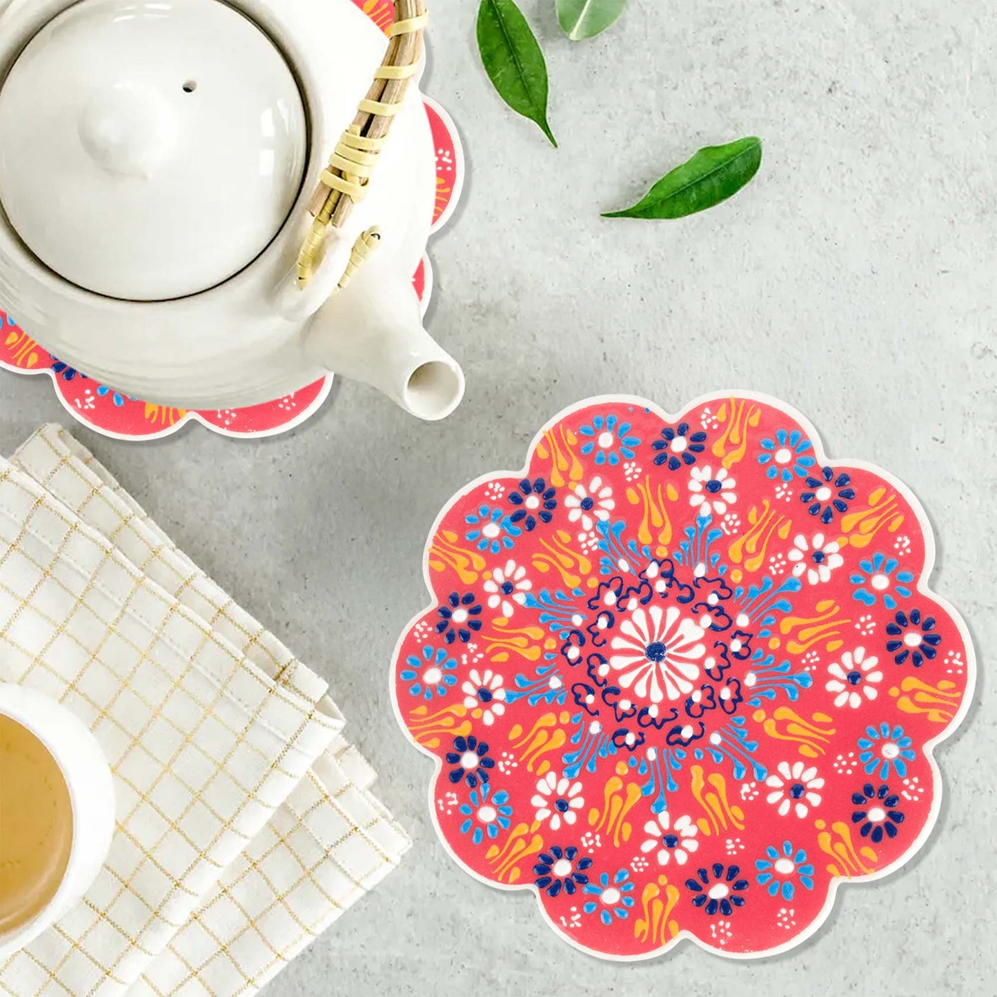 Colorful floral trivet on a gray surface with a teapot and cup.