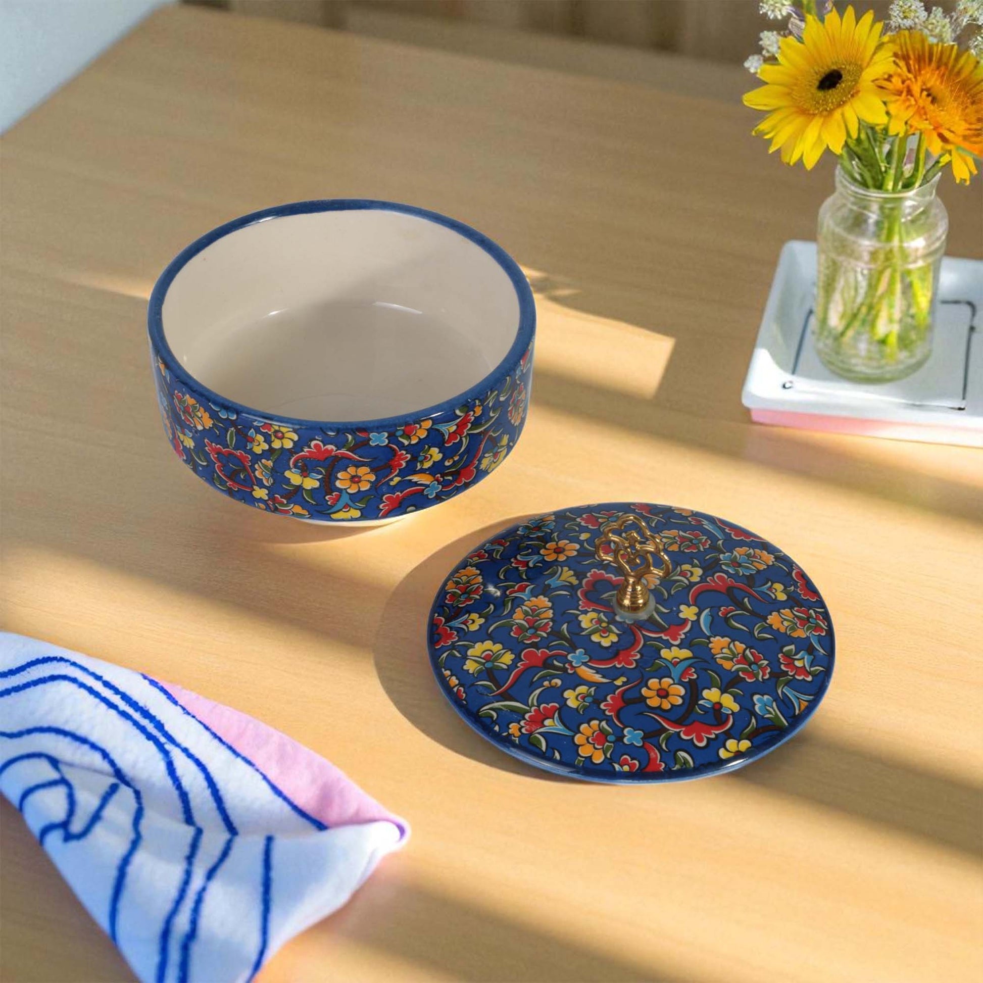 Ceramic sugar bowl with floral design on a wooden table with flowers in the background